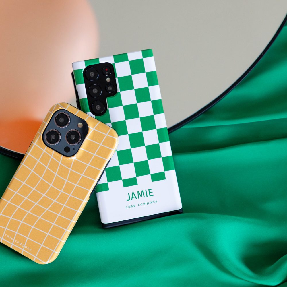 Divi izturīgi vāciņi: dzeltens rūtains vāciņš iPhone tālrunim un zaļš vāciņš kvadrātu rakstā ar vārdu Jamie